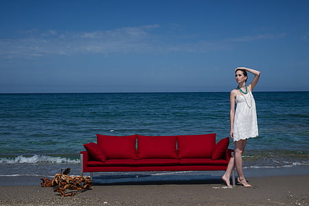 woman in white spaghetti strap mini dress standing beside red couch thumbnail