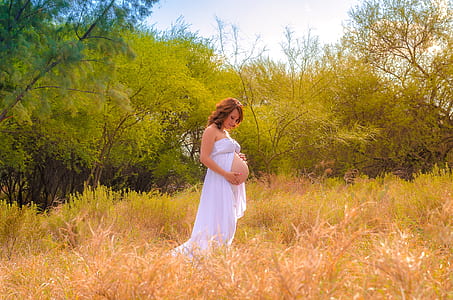 pregnant woman wearing white dress standing on grass thumbnail