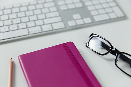 Computer keyboard, notepad and glasses on a white office desk thumbnail