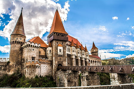 brown and orange concrete castle near bridge surrounded with trees under blue and cloudy sky thumbnail