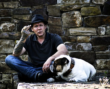 man sitting on concrete surface beside English bulldog at daytime thumbnail