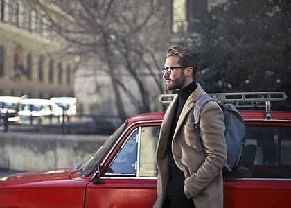 man wearing brown trench coat beside red car during daytime thumbnail