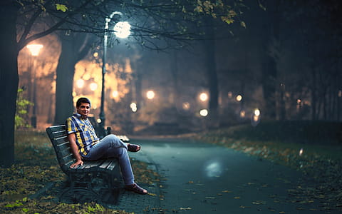 Man in Blue Denim Jeans Sitting Down by Wooden Bench Near Post Lamp Lighted thumbnail