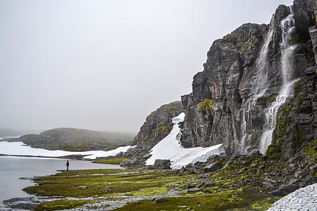 gray rocky cliff with waterfall near body of water surrounded by ice thumbnail