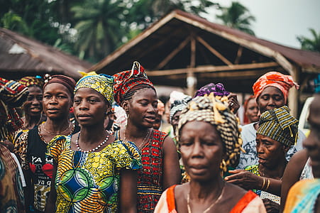 people in dress gather near brown wooden house thumbnail