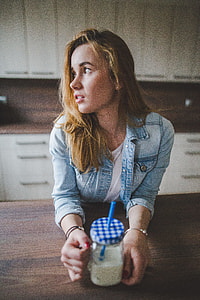 woman wearing blue denim jacket holding jar near wooden table thumbnail
