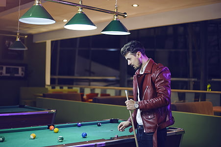 man holds cue stick near green billiard table thumbnail