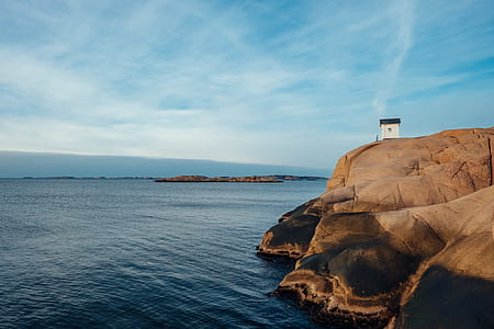 man standing standing in front of white concrete house placed on mountain cliff in front of ocean under cloudy sky thumbnail
