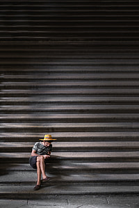 photo of man in brown wicker hat, gray T-shirt, and black shorts sitting on staircase thumbnail