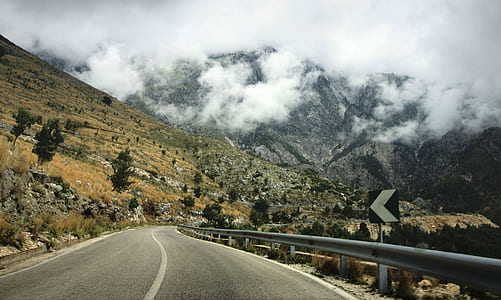 Concrete Road Near Cliff and Hill during Daytime thumbnail