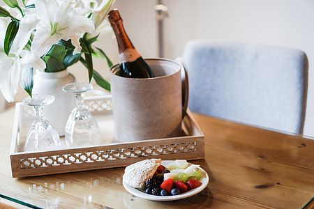 wine bottle on container near two wine glasses on tray with variety of fruits on ceramic saucer thumbnail