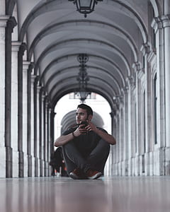 man holding black smartphone sitting near gray concrete pillars thumbnail