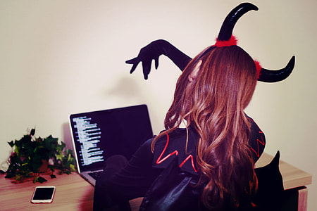 woman in black and red devil costume sitting in front of black laptop computer thumbnail