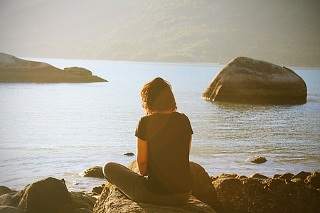person sitting on top of stone near shore during daytime thumbnail