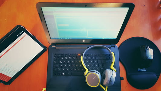 black laptop computer, wireless mouse, tablet computer, and yellow headphones on top of brown wooden furniture thumbnail
