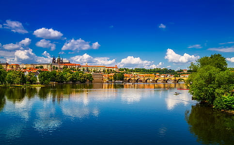 suspension bridge surrounded by water and trees under white clouds and blue sky thumbnail
