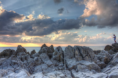 person standing on top of gray large rocks thumbnail