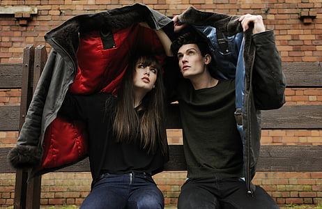 man and woman holding jackets sits near brown brick wall during daytime thumbnail