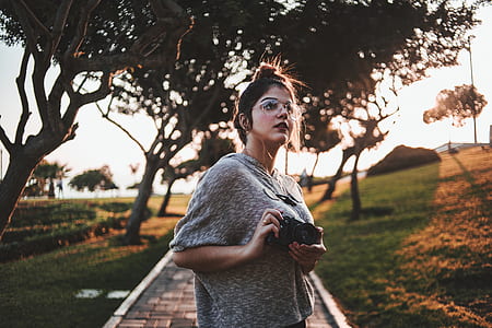 woman holding black camera near green leafed tree at daytime thumbnail
