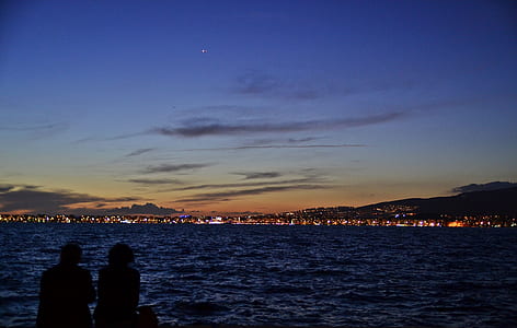 two person sitting on bench looking on body of water thumbnail