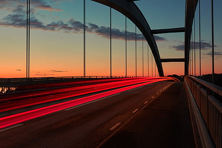 time lapse photography of vehicle travelling on bridge during orange sunset thumbnail