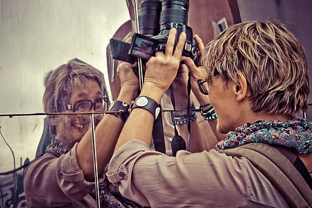 smiling man leaning on mirror while holding black DSLR camera thumbnail