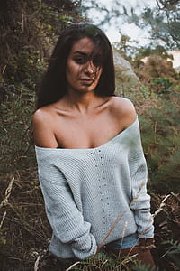 woman wearing gray knit off-shoulder sweater surrounded by green leafed plants thumbnail