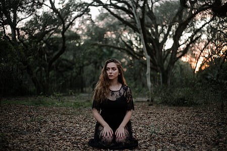 woman in black lace short-sleeved dress kneeling on brown dried leaves under a tree during sunset thumbnail