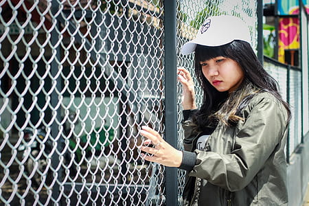 Woman Wearing Grey Bomber Jacket Leaning Near Grey Wire Fence thumbnail