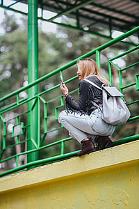 Blonde woman in a black jacket and ripped jeans by a green handrail thumbnail