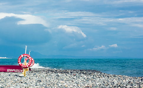 Red and White Ring Signage on Gravel Near Body of Water Under Blue and White Sky thumbnail