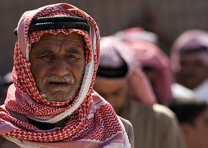 selective focus portrait photo of man in red keffiyeh with black agal headdress thumbnail