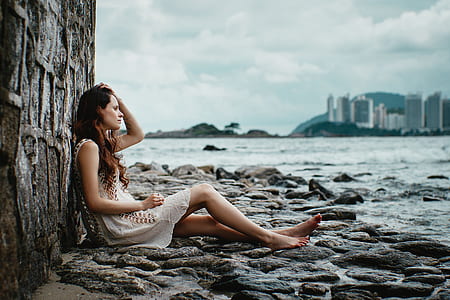 woman sitting on gray rocks beside body of water during daytime thumbnail