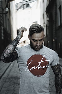 man with full-sleeved arm tattoo in gray crew-neck shirt with red and white print walking on street at daytime thumbnail
