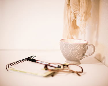 gray tea cup near black eyeglasses and pen on notebook thumbnail