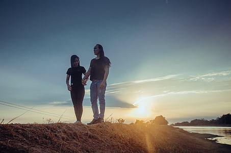 two women on top of hill near body of water at golden hour thumbnail