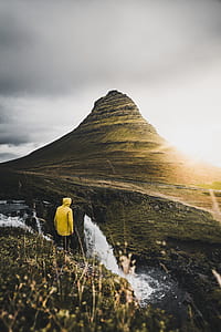 person in yellow hooded jacket standing with brown mountain background thumbnail
