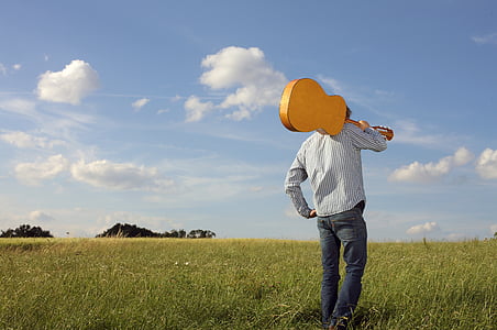 person holding guitar standing on green grass field thumbnail