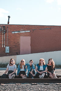 five women sitting on train tracks near brown concrete building during daytime thumbnail