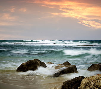 ocean waves bashing rocks on sea shore at sunset thumbnail