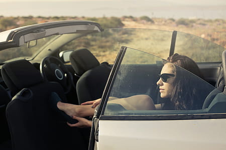 Young Woman In Black Miniskirt And Sunglasses Removing Her Sandals While Sitting In Convertible Car thumbnail