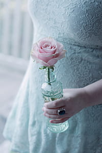 woman in white lace dress holding a pink rose in clear glass vase thumbnail