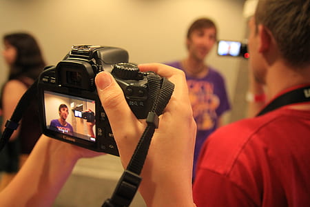 person taking photo of man wearing purple shirt using black Canon camera thumbnail
