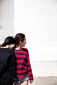 woman leaning head on other woman's neck near white concrete wall during daytime thumbnail