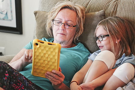 Woman Holding Tablet Lying Beside Girl Wear Eyeglasses thumbnail