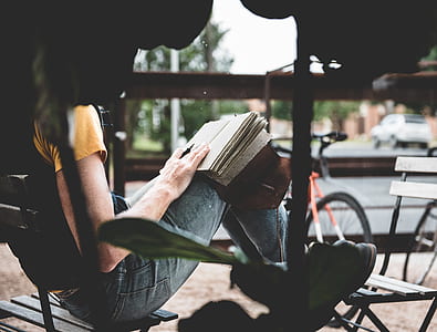 selective focus photography of woman reading book sitting on chair near road during daytime thumbnail