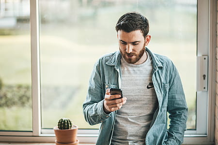 man leaning near window holding phone thumbnail