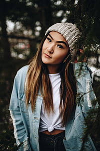 woman touching her knitted cap near green leafed tree thumbnail