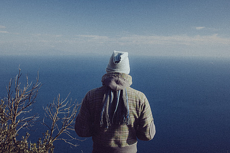 man wearing hooded jacket and gray cap overlooking large blue body of water during daytime thumbnail