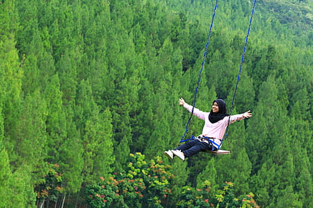 woman swinging over green leafed tree during daytime thumbnail